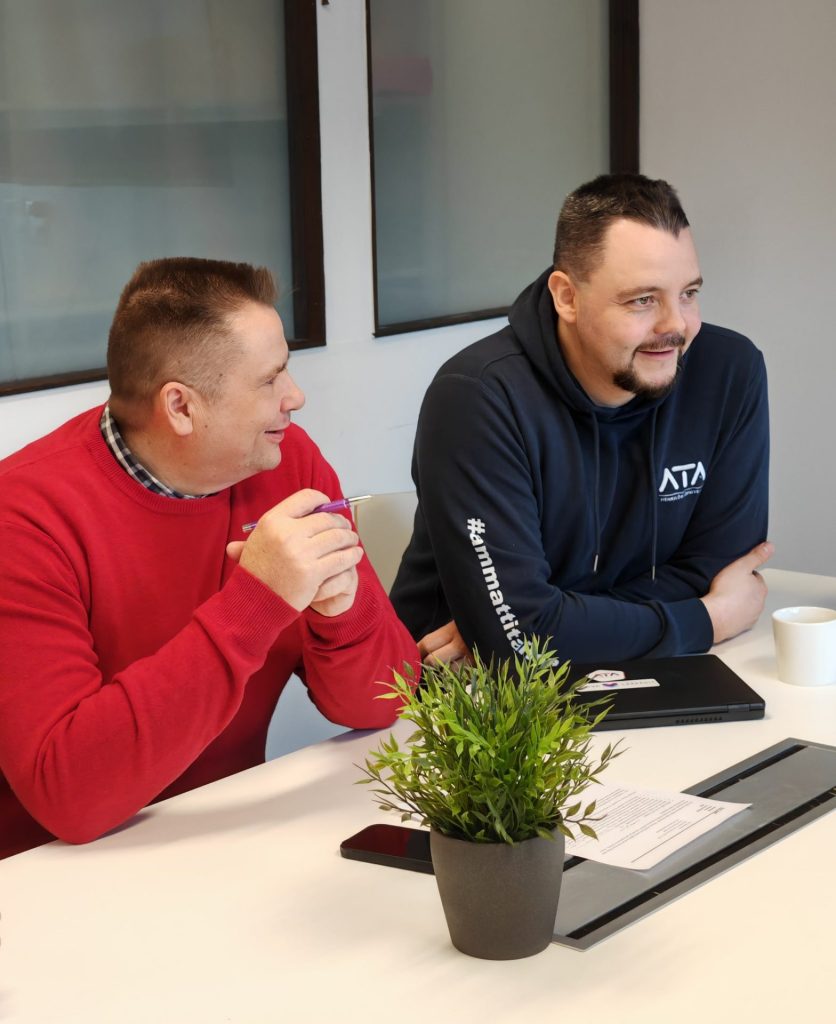 Harri ja Janne-Pekka istuvat pöydän ääressä palaverissa.